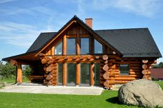 a log cabin sits on the grass next to a large rock in front of it