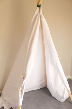 a white teepee sitting on top of a floor next to a wooden stick and wall