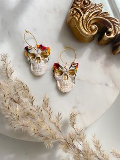 two pairs of skull shaped earrings sitting on top of a white plate next to a plant