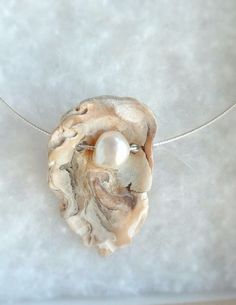 a necklace with a white pearl in the center on a silver chain that is laying on top of a table