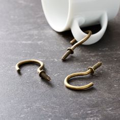 a pair of gold colored metal hooks sitting on top of a table next to a cup