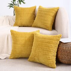 two yellow pillows sitting on top of a white couch next to a wicker basket