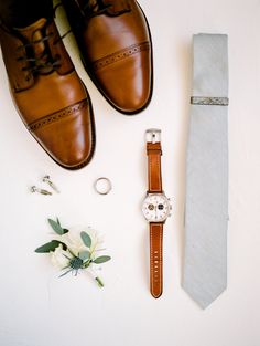 a tie, watch and boutonniere laid out on a white surface next to a pair of shoes