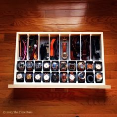 a wooden shelf filled with lots of watches on top of a hard wood floor next to a pair of black shoes