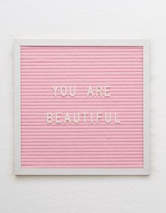 a pink sign that says you are beautiful on the wall next to a white frame