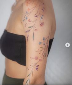 a woman's arm with flowers and leaves on her left shoulder, behind her is a black bra