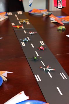 toy airplanes are lined up on the table to race down the road as people watch