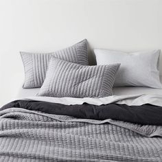 an unmade bed with grey and white pillows