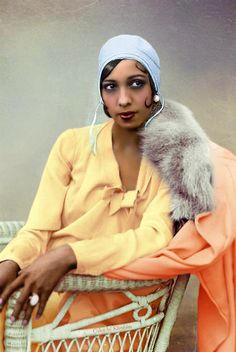 a woman sitting on a chair with a fur stole around her neck and wearing a head scarf