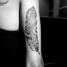 a black and white photo of a person with a feather tattoo on their arm