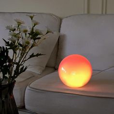 a vase with flowers sitting on a table next to a white couch and lamp in front of it