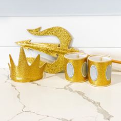 gold crown cups with matching napkins and toothbrush on marble countertop next to white wall