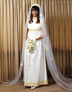 a woman in a white wedding gown and veil with flowers on her head standing next to a curtain