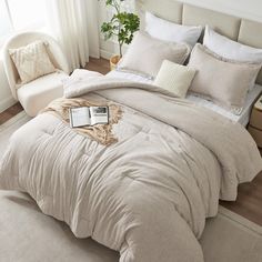 a bed with white sheets and pillows in a room next to a chair, potted plant and window