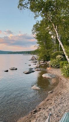 a bench sitting on the shore of a lake next to some trees and rocks in the water