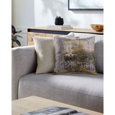 a grey couch with two pillows on it and a book in front of the couch