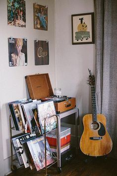 a room with a guitar, record player and various records on the shelf next to it