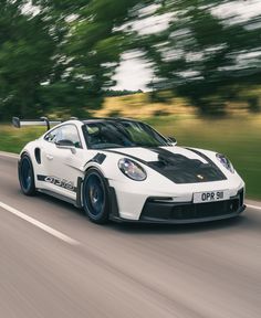 a white porsche sports car driving down the road with trees in the backgroud