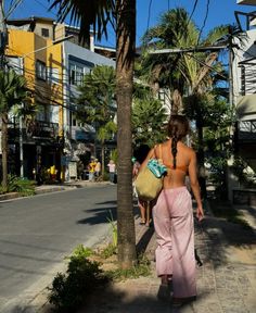 a woman walking down the street carrying a basket in her hand and wearing pink pants