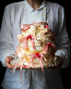 a man holding a cake with pink ribbons on it's sides and the top layer is covered in white frosting