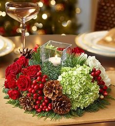 a christmas centerpiece with pine cones, greenery and red flowers on a table