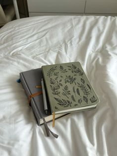 two notebooks sitting on top of a bed next to each other with pencils sticking out of them