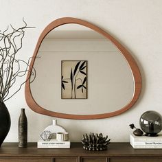 a mirror sitting on top of a wooden dresser next to a vase with plants in it