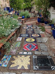 a walkway made out of mosaic tiles in a garden with potted plants on either side