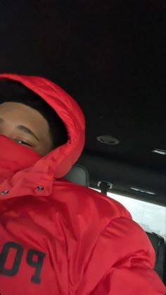 a man wearing a red jacket and hood in the back of a car