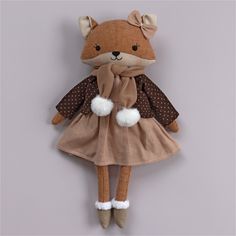 a stuffed animal wearing a brown dress and white shoes is hanging on the wall in front of a gray background