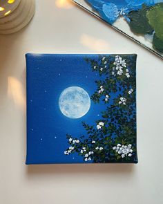 a painting on a white table with a blue sky and full moon in the background