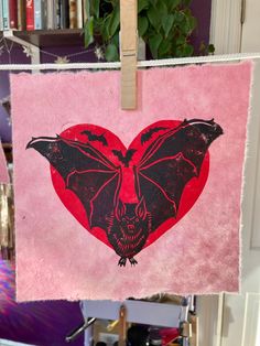 a red heart with a bat on it hanging from a clothes line in front of a bookshelf