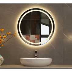 a bathroom sink with a round mirror above it and flowers in a vase on the counter