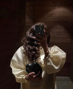 a woman taking a selfie with her cell phone in front of her, wearing a white dress and holding a black heart shaped case