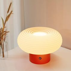 an orange table lamp sitting on top of a white counter next to a vase with flowers