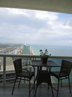 two chairs and a table on a balcony overlooking the ocean with buildings in the background