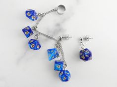 🎲 Carry your love of gaming with you wherever you go when you wear these mini blue swirl polyhedral dice chained ear cuffs! All seven polyhedral dice are present on the chain and dangling from the posts. These are the perfect fancy and funky accessory for game night, cons, or wherever you feel like showing off your love of gaming and dice. This is a mismatched set with a cuff designed for the right ear (but can be worn on the left as well) with six dice and a post for the other ear with one D20. 🎲 Also available in more colors, please check my other listings for availability. 🎲 Hypoallergenic stainless steel cuff is flexible enough to size to your ear. 🎲 Each order comes ready-to-gift in a white, cotton-filled box and black satin bag. 🎲 We understand accidents happen. If something hap Weird Earrings Aesthetic, Cheap Novelty Blue Earrings, Quirky Blue Earrings For Gift, Handmade Blue Novelty Earrings, Dnd Jewelry, Geek Aesthetic, 20 Sided Dice Earrings, Dice Accessories, Weird Earrings