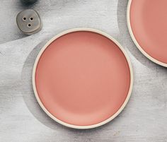 two pink plates sitting on top of a table next to a pair of grey buttons