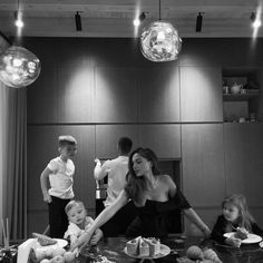 a black and white photo of people around a dining room table with food on it