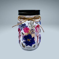 a glass jar with flowers painted on the lid and string tied to it's side