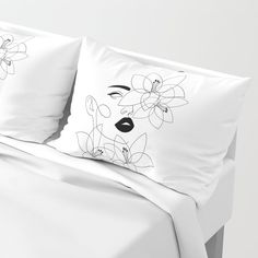 a white bed topped with two pillows next to a pillow case filled with flowers and leaves