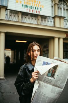 a woman reading a newspaper in front of a theater