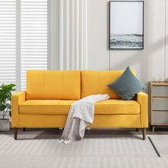 a living room with a yellow couch and some plants on the side table next to it