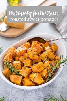 a white bowl filled with roasted potatoes and topped with herbs next to sliced bread on a cutting board