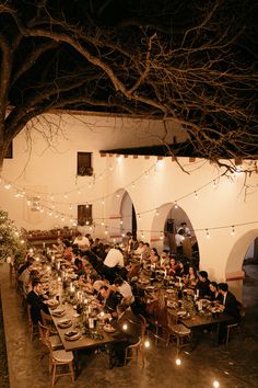 a group of people sitting at tables with candles in front of them and lights hanging from the ceiling