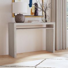 a console table with a lamp and vase on it in front of a painting hanging on the wall