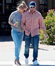 the man and woman are walking down the street together, holding drinks in their hands