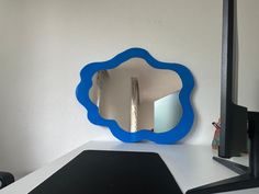 a blue mirror sitting on top of a white desk next to a black computer monitor