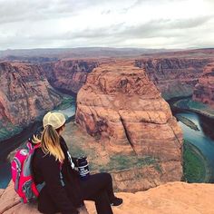 a woman sitting on the edge of a cliff overlooking a river and canyon in grand canyon national park