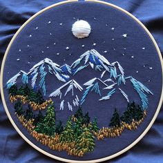 an embroidery project with mountains and pine trees on it, in the middle of blue fabric